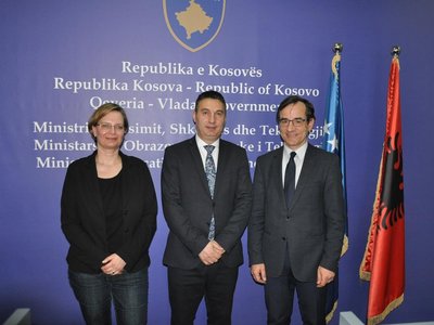 Herr Shyqiri Bytyqi (MEST), Frau Veronika Nitsche (WUS Austria) und Ulrich Hörmann posieren vor blauem Hintergrund mit Kosovo Wappen