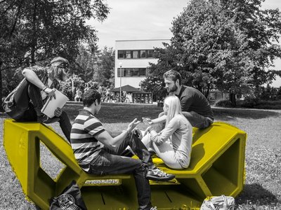 Studierende auf einem Enzi-Möbel im Garten der Universität Klagenfurt