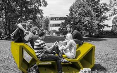 Studierende auf einem Enzi-Möbel im Garten der Universität Klagenfurt