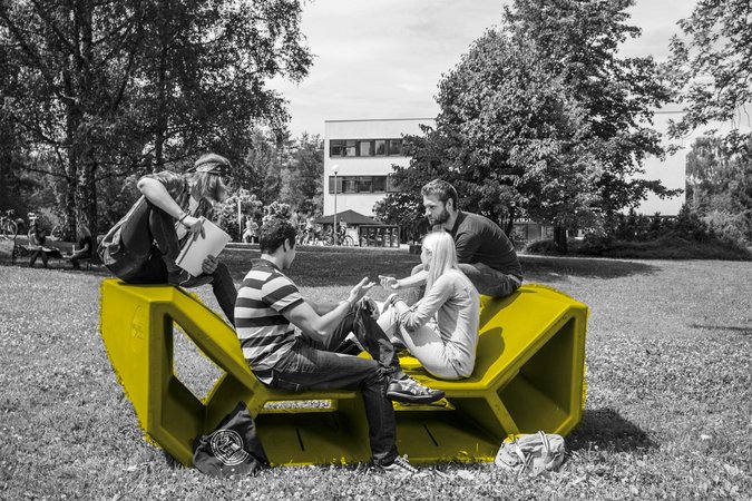 Studierende auf einem Enzi-Möbel im Garten der Universität Klagenfurt