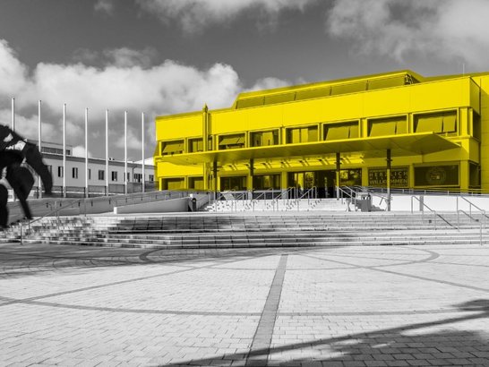 Schwarzweiß-Foto der Universität Klagenfurt mit gelben Highlights