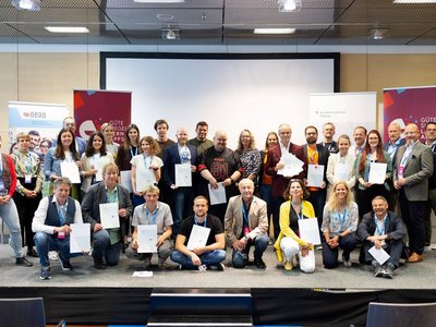 Gruppenbild mit ca. 35 Personen auf einer Bühne, die meisten halten ein Zertifikat in der Hand