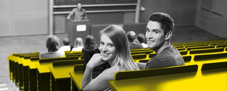 Eine Studentin und ein Student sitzen im Hörsaal und lachen in die Kamera. 