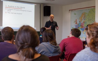 A lecturer speaks to students in a lecture hall with a map on the wall.