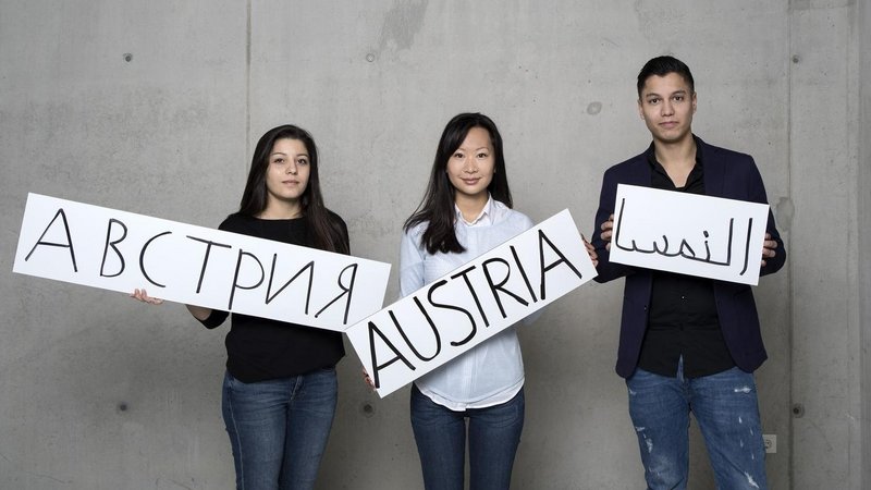 Drei Personen mit Österreichschildern in verschiedenen Sprachen aus Karton