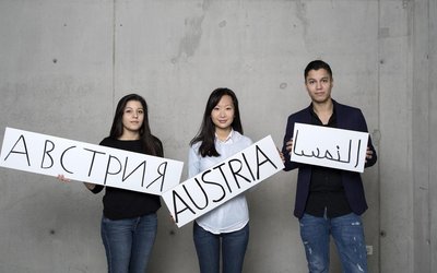 Drei Personen mit Österreichschildern in verschiedenen Sprachen aus Karton