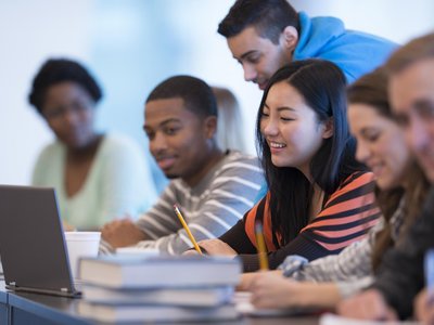 Studierende unterschiedlicher Ethnien mit Büchern und Laptop bei einer Gruppenarbeit