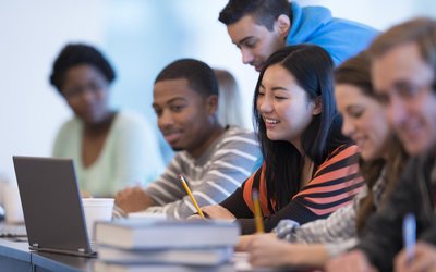 Studierende unterschiedlicher Ethnien mit Büchern und Laptop bei einer Gruppenarbeit